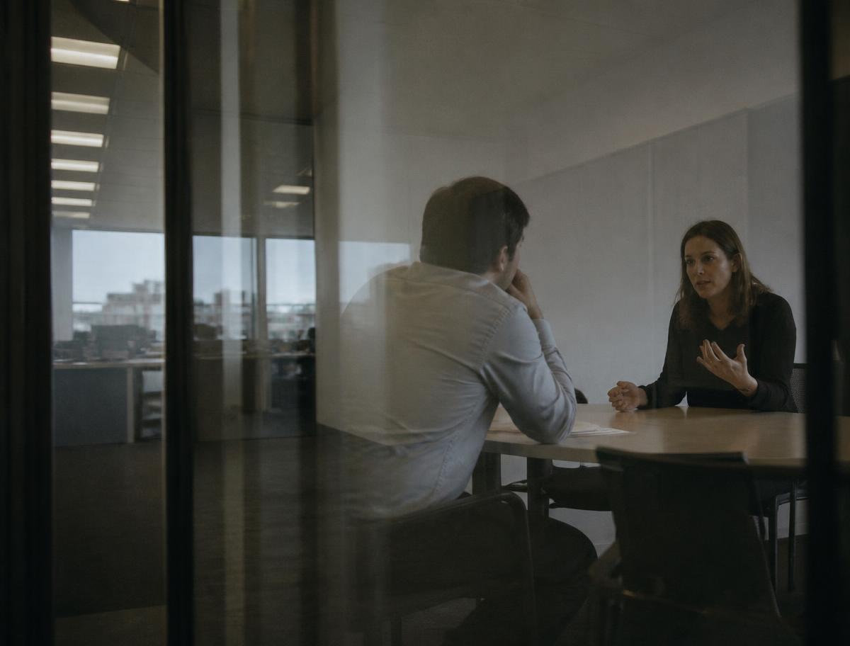 Two colleagues in a private meeting room seen through glass